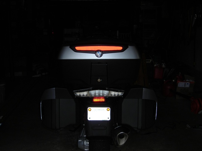 The back end of the motorcycle and high, red reflector with flash.